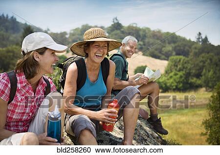 Stock Image - Hikers siting on rock and laughing. Fotosearch