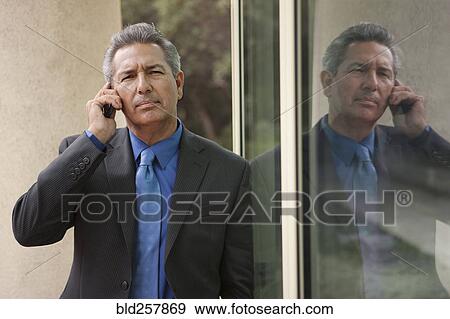 Stock Photo - Hispanic businessman leaning on window talking on cell phone. Fotosearch