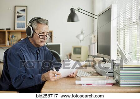Hispanic businessman reading paperwork and listening to headphones View Large Photo Image Stock Photo - Hispanic businessman reading paperwork and listening to headphones. Fotosearch
