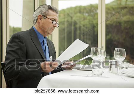 Stock Photograph - Hispanic businessman reading paperwork in restaurant. Fotosearch