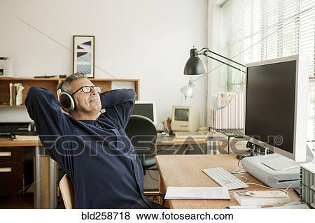Hispanic businessman relaxing at desk and listening to headphones View Large Photo Image Stock Photo - Hispanic businessman relaxing at desk and listening to headphones. Fotosearch