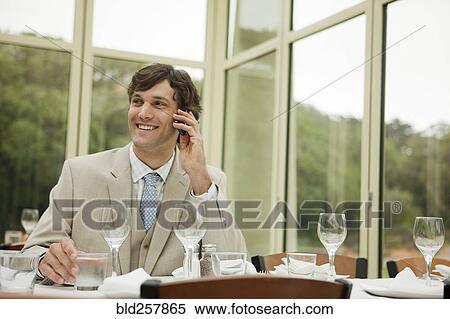 Stock Photography - Hispanic businessman talking on cell phone in restaurant. Fotosearch
