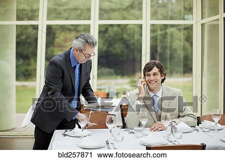 Stock Image - Hispanic businessmen leaning working at table in restaurant. Fotosearch