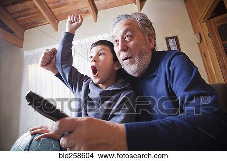 Picture - Hispanic grandfather and grandson cheering for soccer game on television. Fotosearch