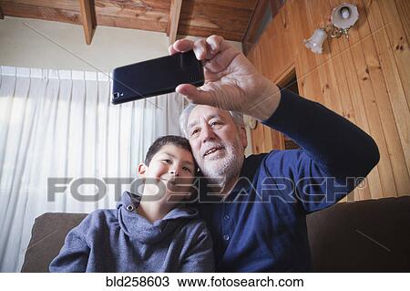 Stock Image - Hispanic grandfather and grandson posing for cell phone selfie. Fotosearch