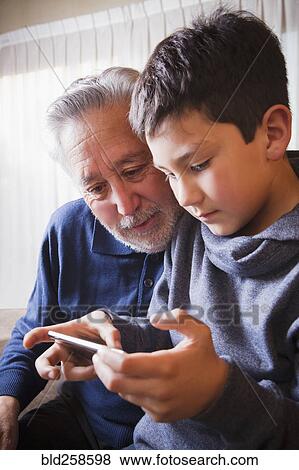 Hispanic grandfather and grandson texting on cell phone View Large Photo Image Stock Photo - Hispanic grandfather and grandson texting on cell phone. Fotosearch