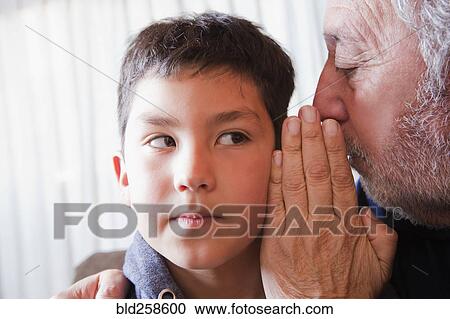 Stock Image - Hispanic grandfather whispering secret to grandson. Fotosearch
