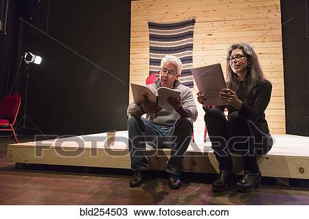 Stock Image - Hispanic man and woman reading scripts on theater stage. Fotosearch