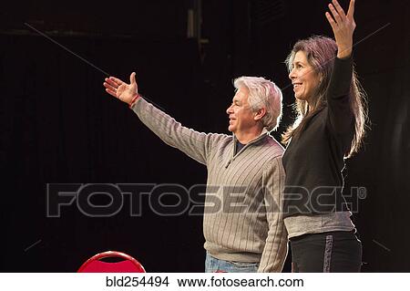 Picture - Hispanic man and woman with arms raised on theater stage. Fotosearch
