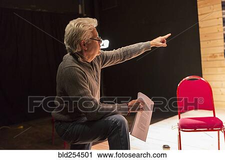 Stock Image - Hispanic man holding script pointing in theater. Fotosearch