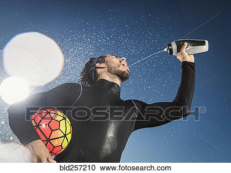 Hispanic man holding soccer ball spraying water into mouth View Large Photo Image Stock Image - Hispanic man holding soccer ball spraying water into mouth. Fotosearch