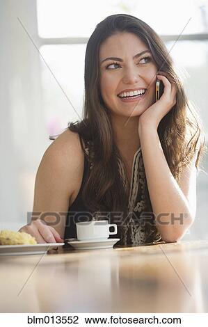 Stock Image - Hispanic woman drinking coffee and talking on cell phone. Fotosearch