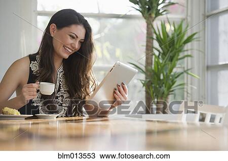 Hispanic woman drinking coffee and using digital tablet View Large Photo Image Stock Image - Hispanic woman drinking coffee and using digital tablet. Fotosearch
