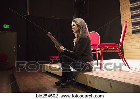 Stock Image - Hispanic woman reading script on theater stage. Fotosearch