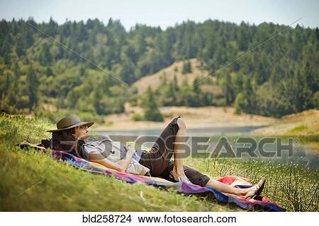 Picture - Hispanic woman relaxing on blanket near river. Fotosearch