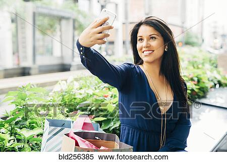 Hispanic woman sitting on bench posing for cell phone selfie View Large Photo Image Stock Photography - Hispanic woman sitting on bench posing for cell phone selfie. Fotosearch