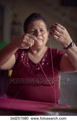 Stock Image - Hispanic woman weaving fabric on loom. Fotosearch