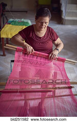 Stock Image - Hispanic woman weaving fabric on loom. Fotosearch