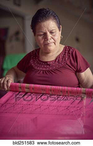 Stock Image - Hispanic woman weaving fabric on loom. Fotosearch