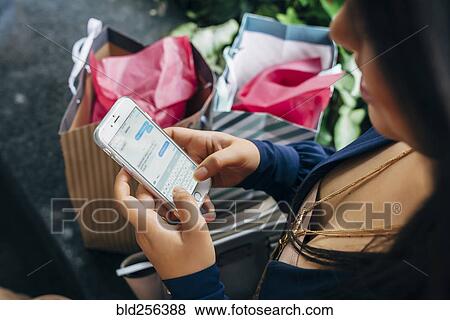 Stock Photo - Hispanic woman with shopping bags texting on cell phone. Fotosearch