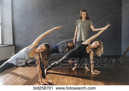 Stock Image - Instructor watching Caucasian women stretching arms in yoga class. Fotosearch