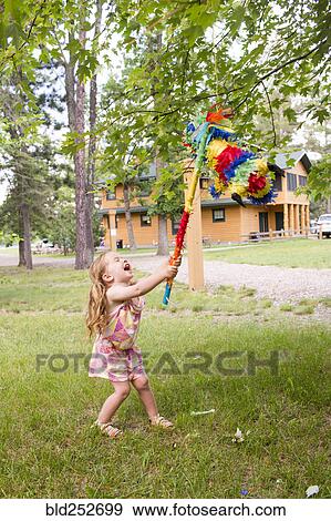 Stock Photo - Laughing Caucasian girl hitting pinata outdoors. Fotosearch