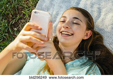 Stock Photo - Laughing Caucasian girl laying on blanket texting on cell phone. Fotosearch