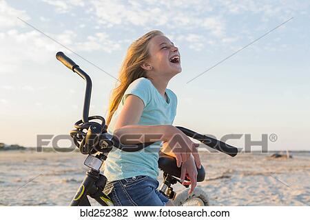 Stock Image - Laughing Caucasian girl leaning on bicycle at beach. Fotosearch