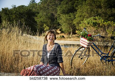 Stock Photo - Laughing Caucasian woman sitting near bicycle. Fotosearch