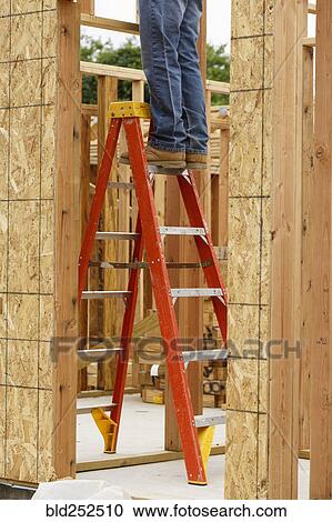 Stock Image - Legs of Caucasian man on ladder at construction site. Fotosearch