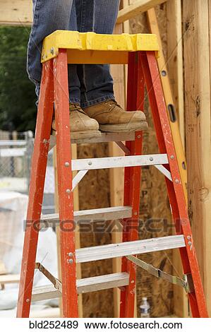 Stock Photo - Legs of Caucasian man standing on ladder at construction site. Fotosearch
