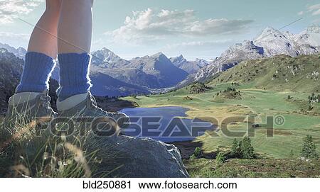 Stock Image - Legs of Caucasian woman standing on rock over valley lake. Fotosearch