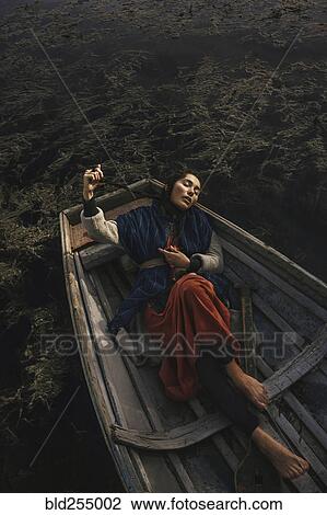 Stock Image - Location woman wearing traditional clothing laying in rowboat. Fotosearch