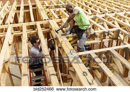 Stock Photograph - Man and woman hammering frame at construction site. Fotosearch