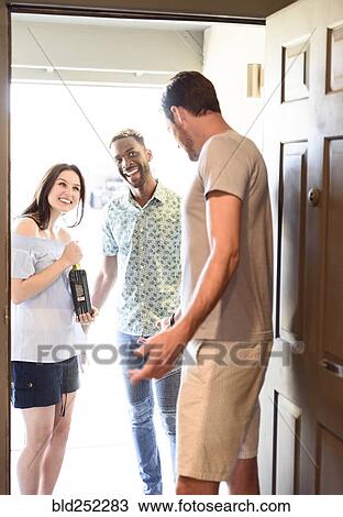 Man greeting couple bringing wine bottle at door View Large Photo Image Stock Image - Man greeting couple bringing wine bottle at door. Fotosearch