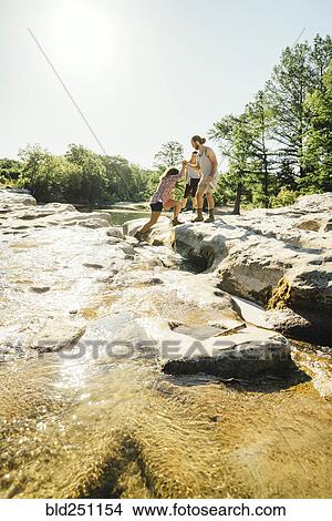 Picture - Man helping woman crossing river. Fotosearch