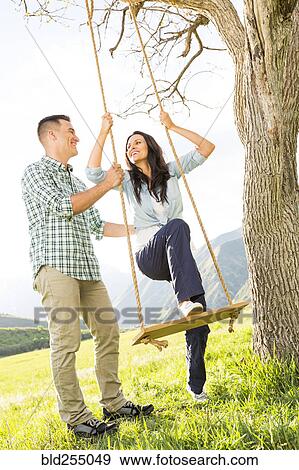 Stock Photo - Man helping woman on tree swing. Fotosearch