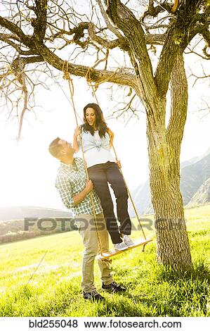 Stock Photo - Man holding woman on tree swing. Fotosearch