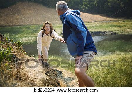 Picture - Man pulling arm of woman up hill near lake. Fotosearch