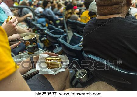 Stock Photo - Man sitting in stadium eating hot dog. Fotosearch