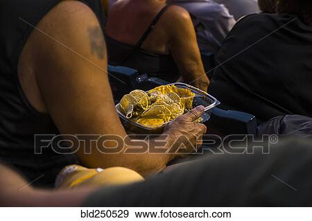 Stock Photo - Man sitting in stadium eating nachos. Fotosearch
