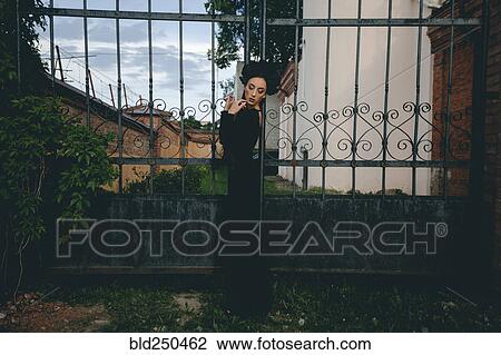 Stock Image - Middle Eastern woman wearing black dress near gate. Fotosearch