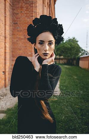 Stock Image - Middle Eastern woman wearing black dress near brick building. Fotosearch