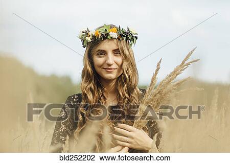 Stock Image - Middle Eastern woman wearing flower crown holding wheat. Fotosearch