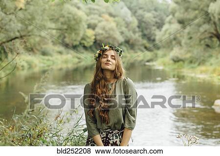 Stock Photo - Middle Eastern woman wearing flower crown near river. Fotosearch