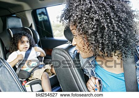 Stock Photo - Mixed race and mother checking daughter in car seat. Fotosearch