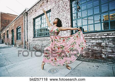 Stock Photo - Mixed race ballet dancer wearing dress on sidewalk. Fotosearch
