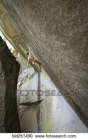 Stock Image - Mixed race boy hanging from rock. Fotosearch