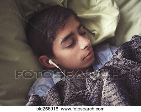 Stock Photography - Mixed race boy laying in bed listening to earbuds. Fotosearch