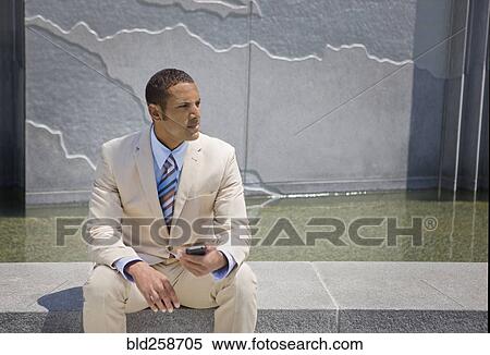 Mixed race businessman sitting outdoors texting on cell phone View Large Photo Image Stock Photography - Mixed race businessman sitting outdoors texting on cell phone. Fotosearch